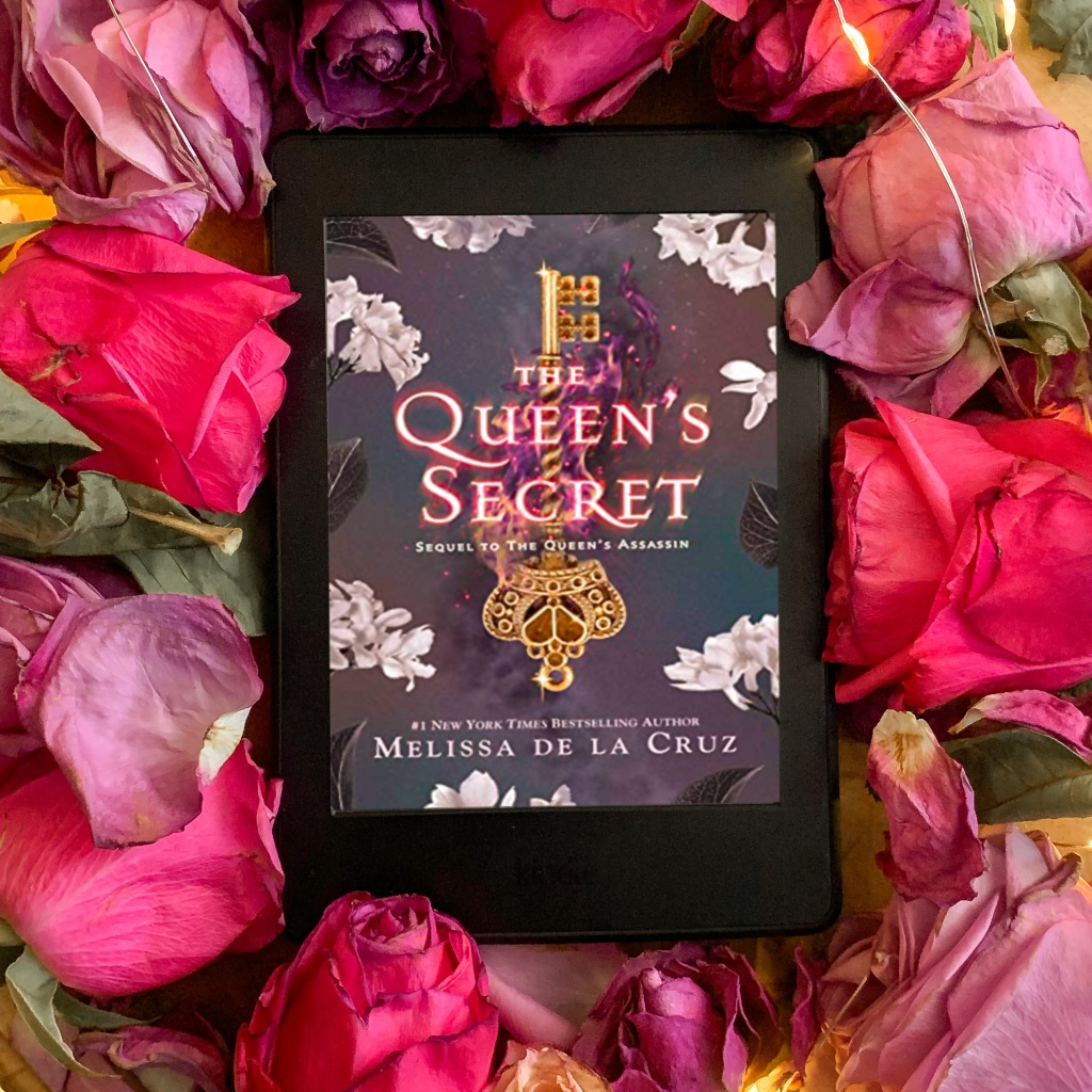 Photo of The Queen's Secret by Melissa De La Cruz, sequel to The Queen's Assassin, on kindle surrounded by roses